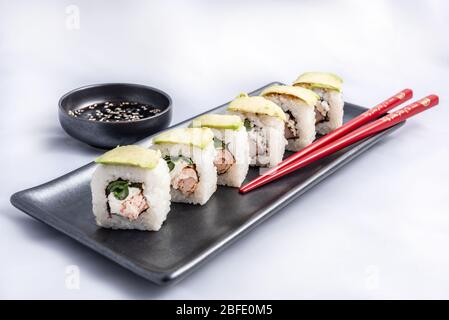 Rotolo di sushi con wrap avocado, salmone alla griglia, formaggio philadelphia e cipolle verdi contenitore nero e bacchette rosse. Foto Stock