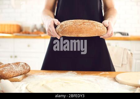 L'uomo bearded di Baker tiene nelle sue mani il pane fresco che sta in piedi nella cucina. Foto Stock