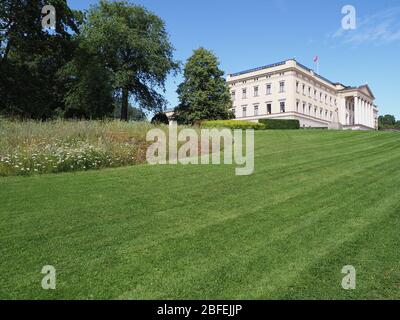 Campo erboso e palazzo nella capitale europea di Oslo nel distretto di Ostlandet in Norvegia, cielo azzurro chiaro in 2019 caldo sole giorno estivo il mese di luglio. Foto Stock