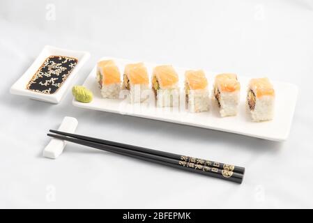 Sushi roll con impacco di salmone rosa, salmone alla griglia, formaggio Philadelphia e avocado. Contenitore bianco e bacchette nere. Foto Stock