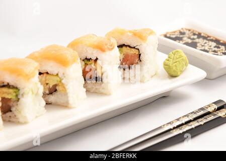 Sushi roll con impacco di salmone rosa, salmone alla griglia, formaggio Philadelphia e avocado. Contenitore bianco e bacchette nere. Foto Stock