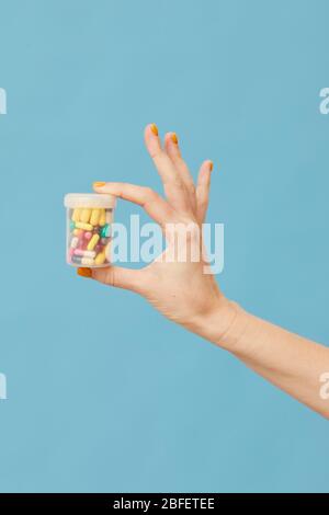 Primo piano del flacone femmina di contenimento della mano con capsule e pillole su sfondo blu Foto Stock