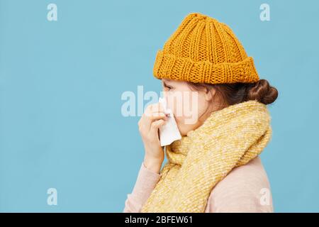 Vista laterale della giovane donna in lana cappello e sciarpa catturati un freddo isolato su sfondo blu Foto Stock