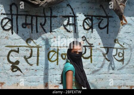 Delhi, India. 17 Aprile 2020. Una ragazza che indossa una maschera facciale come misura preventiva contro la diffusione di coronavirus cammina oltre un coronavirus graffiti durante un lockdown.India a livello nazionale ha registrato un totale di 14,792 casi confermati, 2,045 recuperati e 488 morti dalla malattia del virus corona. Credit: SOPA Images Limited/Alamy Live News Foto Stock