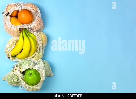 banane di frutta mele arance in sacchi di rete caton su sfondo blu. concetto zero rifiuti. Senza plastica. Foto Stock