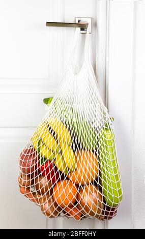 frutta e verdura frutta e verdura appendono sul manico di una porta bianca in un sacchetto a stringa. cipolle zucchine banane pepe arancio. eco zero rifiuti Foto Stock