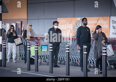 Gli amanti dello shopping si accodano mentre si trovano a distanza sociale per entrare nel Sainsbury’s di Londra indossando maschere facciali Foto Stock