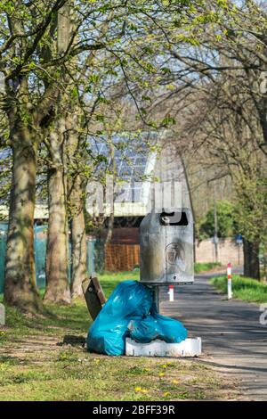 Sacchetti di plastica blu riempiti di immondizia vicino ad un cestino di metallo vuoto possono in un parco pubblico. Inquinamento ambientale, smaltimento illegale dei rifiuti in natura Foto Stock