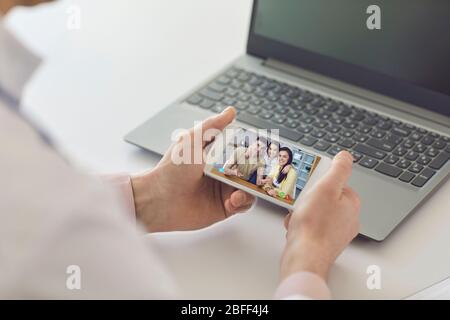 Medico di famiglia online. Il medico di sesso maschile parla con i pazienti dalla famiglia utilizzando il telefono seduto dietro la paglia in ufficio clinico. Foto Stock