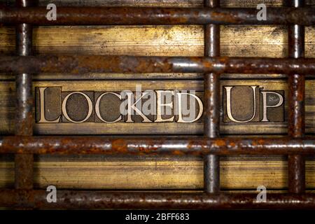 Foto di autentiche lettere typeset in forma bloccato su testo dietro barre arrugginite su vintage textured Grunge rame e oro sfondo Foto Stock