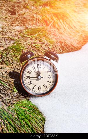 Vecchio orologio retrò sveglia, erba e neve, simboleggia l'arrivo della primavera o inverno Foto Stock