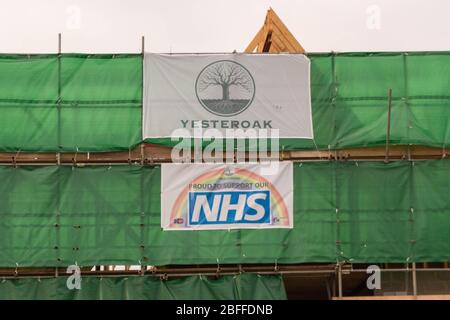Southend-on-Sea, Regno Unito. 18 aprile 2020. Un cantiere a Southend-on-Sea, Essex, presenta striscioni a sostegno del sistema sanitario nazionale durante la pandemia di COVID-19. La segnaletica include un motivo arcobaleno e il messaggio "orgoglioso di supportare il nostro sistema sanitario nazionale", montato su una rete verde intorno all'impalcatura. Catturata durante il blocco, l'immagine riflette la solidarietà della comunità e il riconoscimento aziendale degli operatori sanitari in prima linea. Penelope Barritt/Alamy Live News Foto Stock