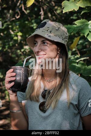 una bella donna modello bere yerba mate infusione mentre si cammina attraverso gli alberi Foto Stock