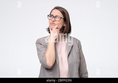 Donna abbastanza matura in occhiali guardando da parte con sguardo pensieroso che fa piano per il futuro. Generazione di idea per progetto di affari. Scatto studio Foto Stock