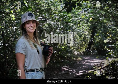 una bella donna modello bere yerba mate infusione mentre si cammina attraverso gli alberi Foto Stock