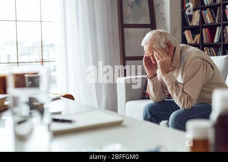 Uomo anziano da solo seduto al tavolo della biblioteca primo piano avendo dolore Foto Stock