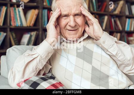 Uomo anziano da solo seduto alla biblioteca infelice avere mal di testa Foto Stock