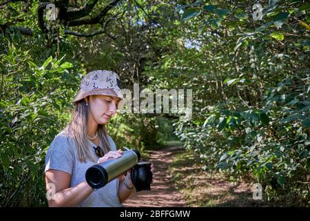 una bella donna modello bere yerba mate infusione mentre si cammina attraverso gli alberi Foto Stock