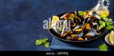 Primo piano di deliziose cozze al vapore in un piatto sfondo blu Foto Stock