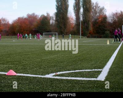 Fuoco selettivo ai coni dell'arker usati per l'addestramento di calcio sul tappeto erboso artificiale verde con i bambini blurry che addestrano lo sfondo Foto Stock