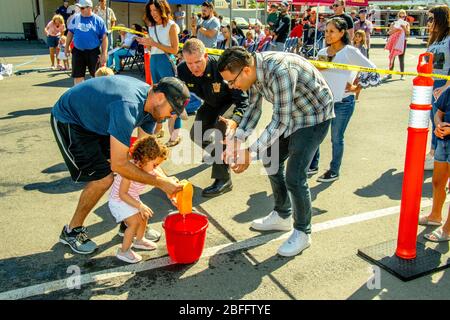 I bambini multirazziali trasportano spugne bagnate come parte di una rievocazione della brigata della benna nell'educazione di rischio della comunità ad una dimostrazione della stazione di fuoco a Costa Mesa, CA. Foto Stock