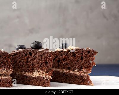 pezzi triangolari di torta al cioccolato con crema di burro su un asse di legno bianco, sfondo grigio, primo piano Foto Stock