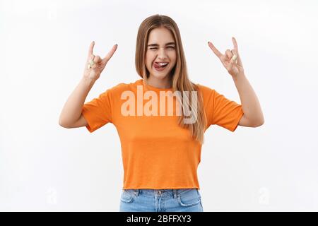 Rock n roll bambino. Felice, ragazza bionda spensierata godendo la festa o il concerto impressionante, mostrando il metallo pesante e la lingua del bastone, sorridente che si annoia gioiosamente, avendo Foto Stock