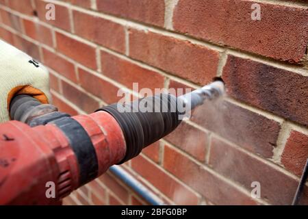 Immagine illustrativa della parete di cavità di isolamento. Un lavoratore di totale isolamento trapani soluzioni di un foro per consentire l'isolamento di rockwool per essere inserita. Foto Stock