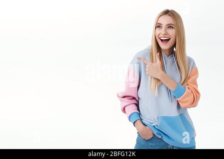 Ritratto di divertito, felice sorridente ragazza bionda che punta il dito a sinistra e guardando entusiasta alla pubblicità del prodotto, discutere con voi nuovo impressionante Foto Stock