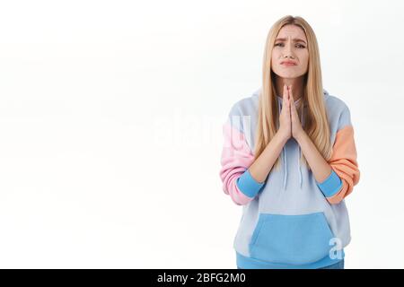 Ritratto di giovane bionda speranzosa in felpa con cappuccio, premere insieme le mani, chiedere aiuto o favore, ha bisogno di qualcosa di male, pregando di prestare alcuni Foto Stock