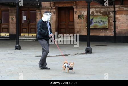 Londra, Regno Unito. 18 Aprile 2020. Giorno ventisei di Lockdown a Londra. Un uomo, in maschera facciale e guanti, cammina il suo cane oltre il Palace Theatre che avrebbe dovuto mostrare Harry Potter e il bambino maledetto. Il paese è bloccato a causa della pandemia di Coronavirus COVID-19. La gente non è autorizzata lasciare la sede tranne per shopping di alimento minimo, trattamento medico, esercitazione - una volta al giorno e lavoro essenziale. COVID-19 Coronavirus lockdown, Londra, Regno Unito, il 18 aprile 2020 Credit: Paul Marriott/Alamy Live News Foto Stock