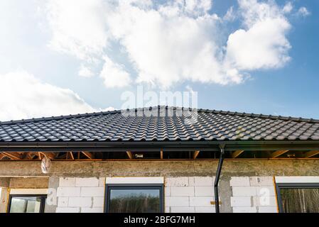 Il tetto di una casa singola-familiare coperta con una nuova piastrella in ceramica antracite contro il cielo blu, capriate visibili. Foto Stock