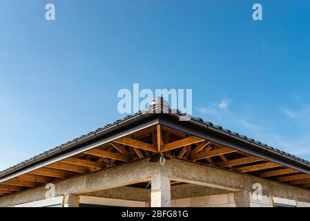 Il tetto di una casa singola-familiare coperta con una nuova piastrella in ceramica antracite contro il cielo blu, capriate visibili. Foto Stock