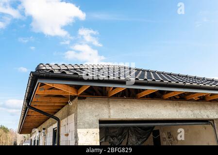 Il tetto di una casa singola-familiare coperta con una nuova piastrella in ceramica antracite contro il cielo blu, capriate visibili. Foto Stock