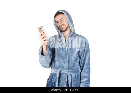 Ritratto di giovane uomo caucasico bearded in blu accappatoio guardare a schermo smartphone isolato su sfondo bianco. Informazioni sulla messaggistica per smartphone Foto Stock