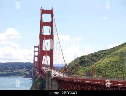 Traffico sul Golden Gate Bridge, traffico leggero durante la CoVID 19 pandemic casa isolamento città in tutta la città. Cielo blu nuvoloso sullo sfondo, verde erboso Foto Stock