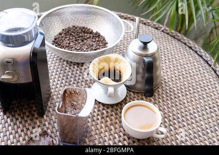 Una tazza di caffè sul tavolo con chicchi di caffè appena tostati, macinacaffè, filtro antigoccia e bollitore Foto Stock