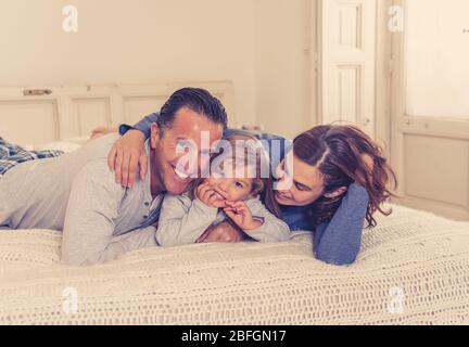 Quarantena COVID-19. Bella famiglia felice rilassarsi e giocare insieme a letto rimanendo a casa durante l'isolamento auto. Madre, padre e toddl carino Foto Stock