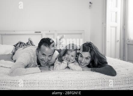 Quarantena COVID-19. Bella famiglia felice rilassarsi e giocare insieme a letto rimanendo a casa durante l'isolamento auto. Madre, padre e toddl carino Foto Stock