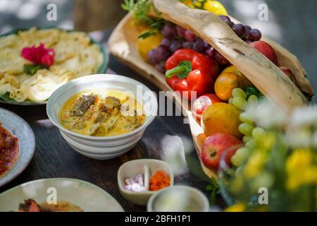 Durante una festa in giardino, il curry di capra viene servito in una ciotola di ceramica su un tavolo di legno. Foto Stock