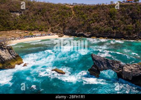 Vista aerea di enormi onde oceaniche, un arco roccioso offshore e spiaggia tropicale (Atuh Beach, Nusa Penida) Foto Stock