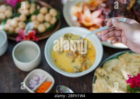 Durante una festa in giardino, il curry di capra viene servito in una ciotola di ceramica su un tavolo di legno. Foto Stock