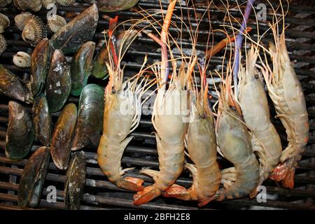 Gamberi a zampe blu Macrobrachium rosenbergii e cozze verdi asiatiche che vengono grigliate al mercato notturno di Hua Hin, Thailandia Foto Stock