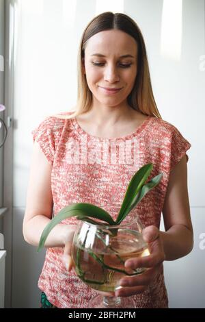 Autentica giovane donna che tiene una pianta di orchidea in un recipiente di vetro con acqua Foto Stock