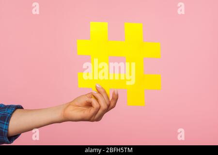 Tendenze dei social media. Primo piano di mano femminile tenendo giallo hashtag segno, condivisione di messaggi tagged, famoso post internet, blogging e contenuto virale. ind Foto Stock