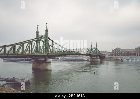 Budapest, Ungheria - 6 novembre 2019: Ponte della libertà sul Danubio in un giorno d'autunno piovoso e nebbioso. Nave da crociera e centro storico sullo sfondo. Foto verticale. Città della capitale ungherese. Foto Stock