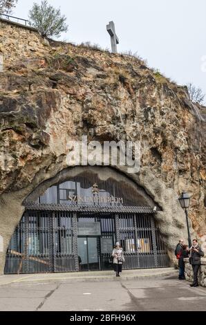 Budapest, Ungheria - 6 novembre 2019: Ingresso alla chiesa della grotta di Gellert Hill, Sziklatemplom. Chiesa rock nella capitale ungherese con la gente. Croce sulla cima della roccia. Foto verticale. Foto Stock