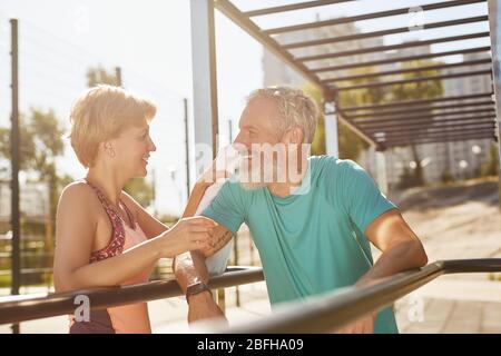 Riposo dopo l'allenamento. Donna sorridente che pulì il sudore del marito dopo aver fatto esercizio allo stadio. Senior Happy Family che lavora insieme nel Foto Stock