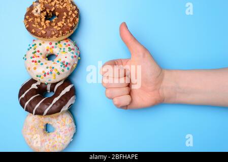 Mi piace donut nel ristorante concetto di reazione positiva. Foto ravvicinata di gustose ciambelle e persone che si alzano pollice isolato su sfondo pastello Foto Stock