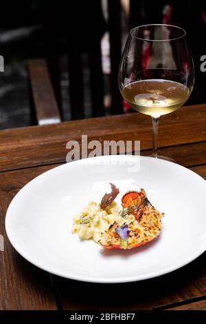 Primo piano con coda di aragosta di boston alla griglia con maccheroni al formaggio fritto, cucina gourmet internazionale con un bicchiere di vino bianco nella stazione a la carte Live Foto Stock